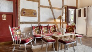 Una stanza con soffitto in legno, una porta rossa, una panca bianca con cuscini floreali e un tavolo bianco.