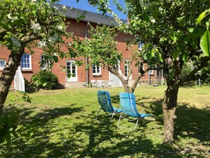 A brick building with a lawn, two blue chairs, and a tree with white flowers.