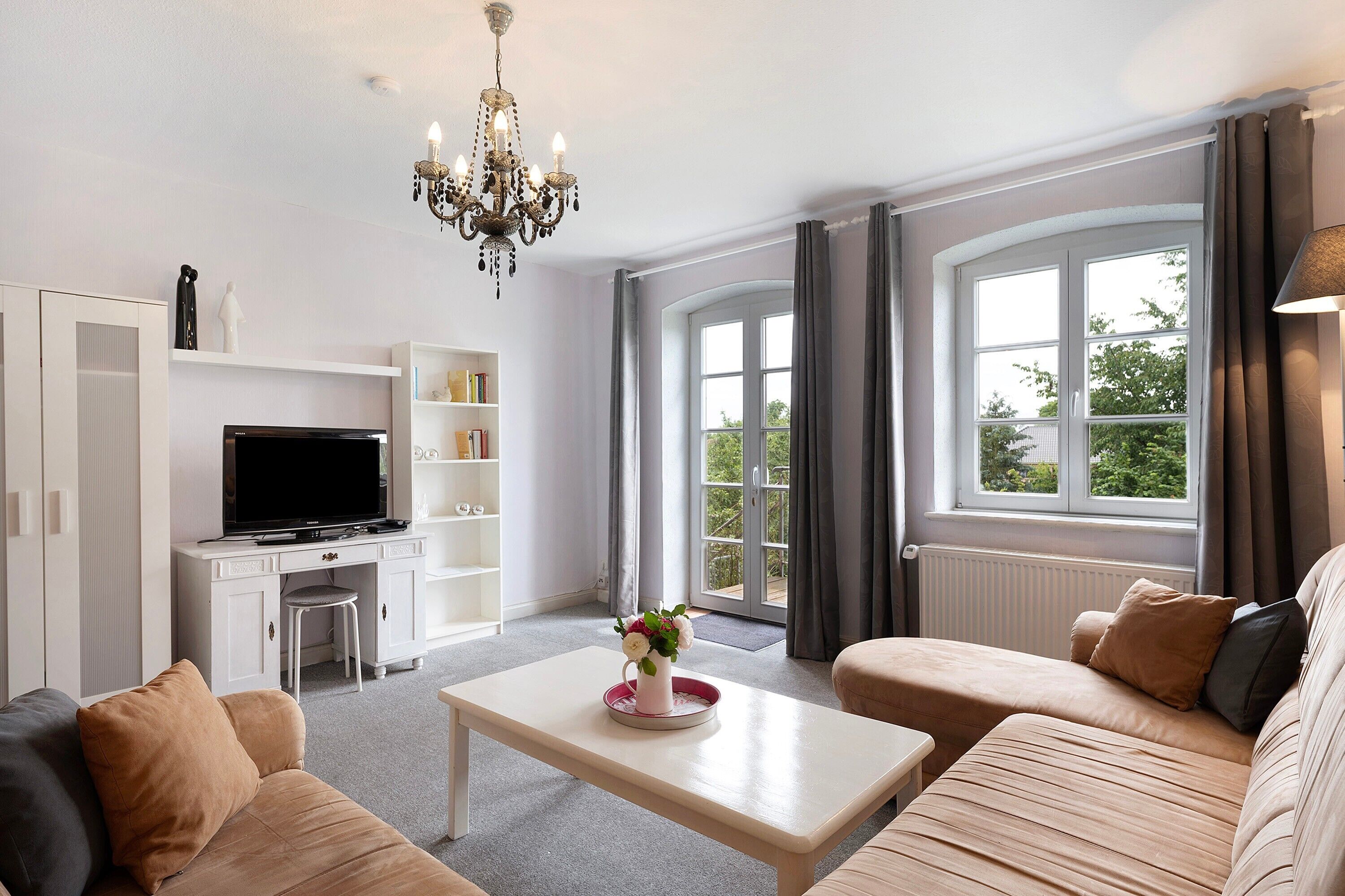 A modern living room with a television, sofa, coffee table, and a chandelier.