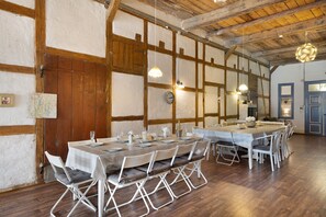 Un espace repas avec une longue table dressée pour le repas, des poutres en bois au plafond et un décor mural rustique.