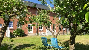 A brick building with a lawn, two blue chairs, and a tree with white flowers.