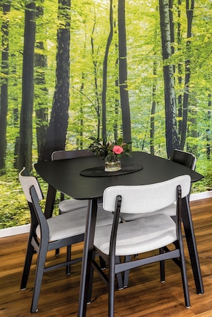 Un coin repas avec une table ronde, quatre chaises et un papier peint représentant une forêt en arrière-plan.