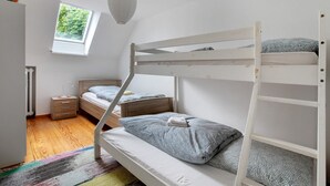 Ein Schlafraum mit Etagenbetten, einem Fenster, einem Schreibtisch und einem farbenfrohen Teppich.