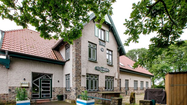 Ein Gebäude mit einer Steinauffassade, zahlreichen Fenstern und einem Schild mit der Aufschrift 'Felsenburg'.