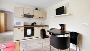 A compact kitchen with a microwave, stove, and sink. There is a dining area with a table and chairs. - Apartment 'Wattwurm' with Wi-Fi (Ahrenviölfeld)