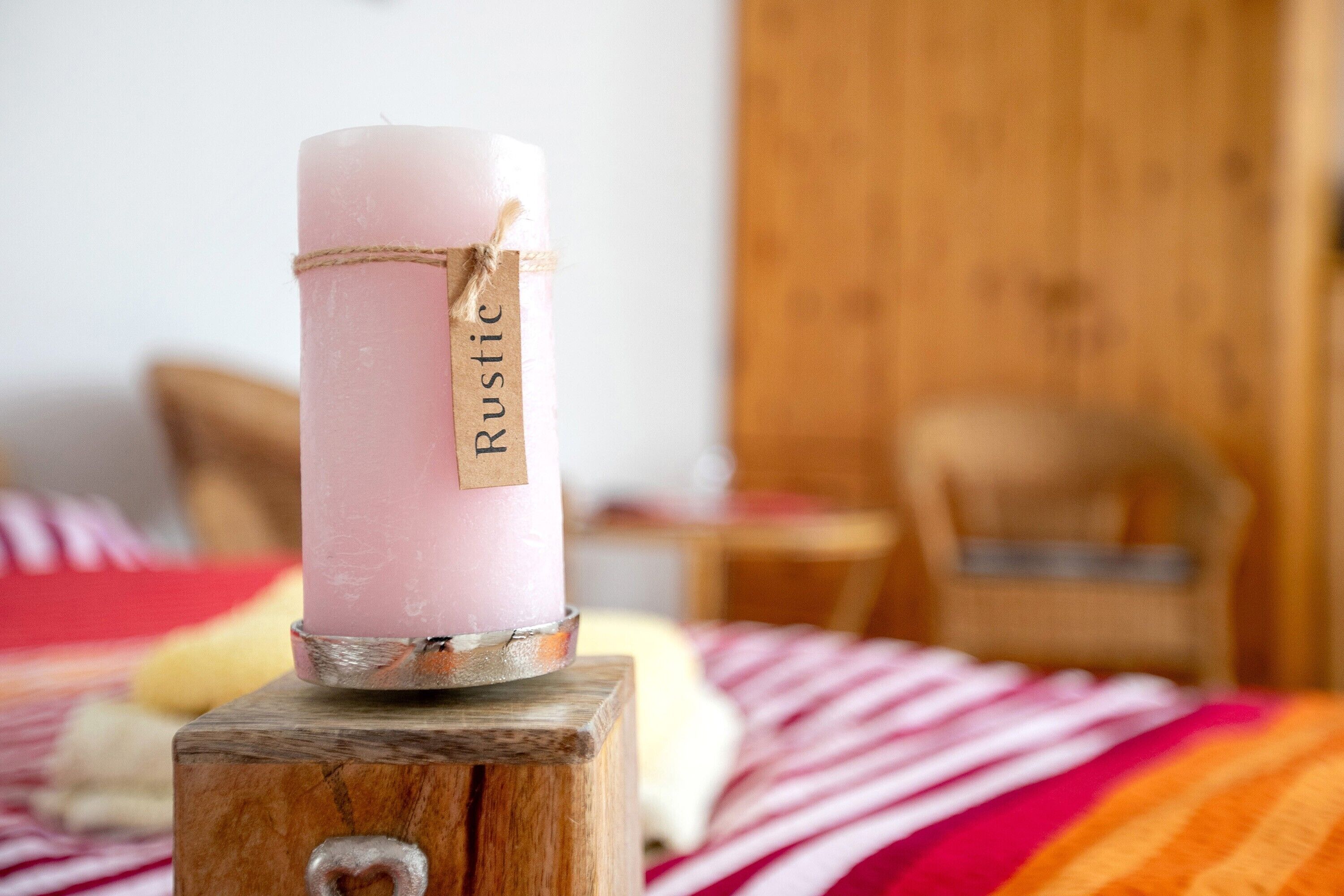 Vaaleanpunainen kynttilä, jossa on puupalikkaan kiinnitettynä etiketti, jossa lukee ”Rustic”.