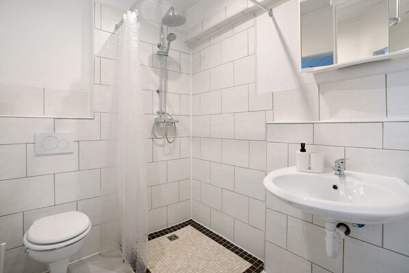 A bathroom with white tiles, a shower, a toilet, and a sink.