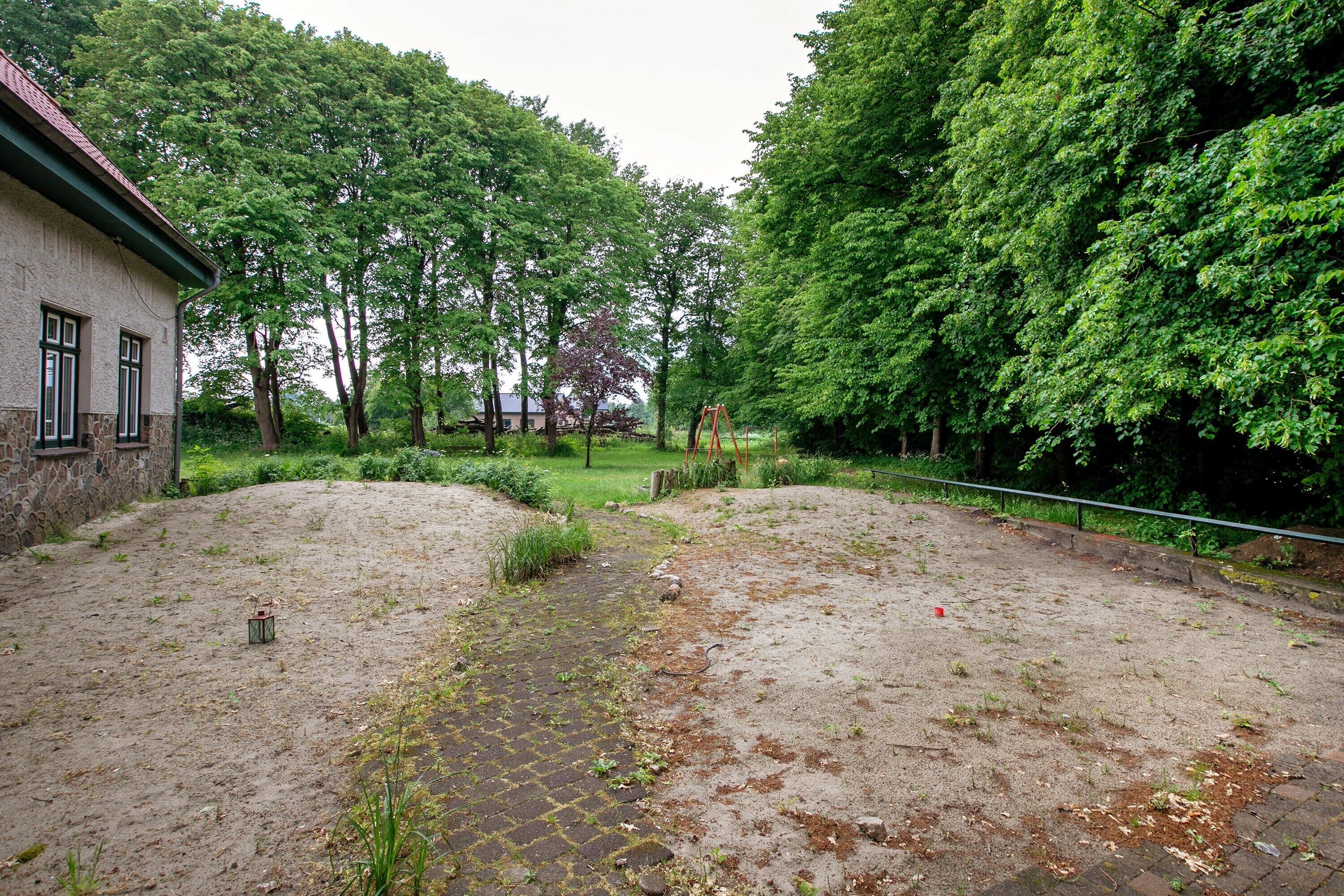 A courtyard with a paved walkway, a stone building, and dense trees.