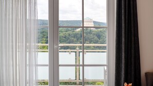 A room with a large window, a view of a lake, and a building in the distance.