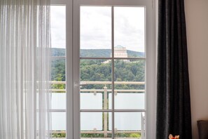 A room with a large window, a view of a lake, and a building in the distance.