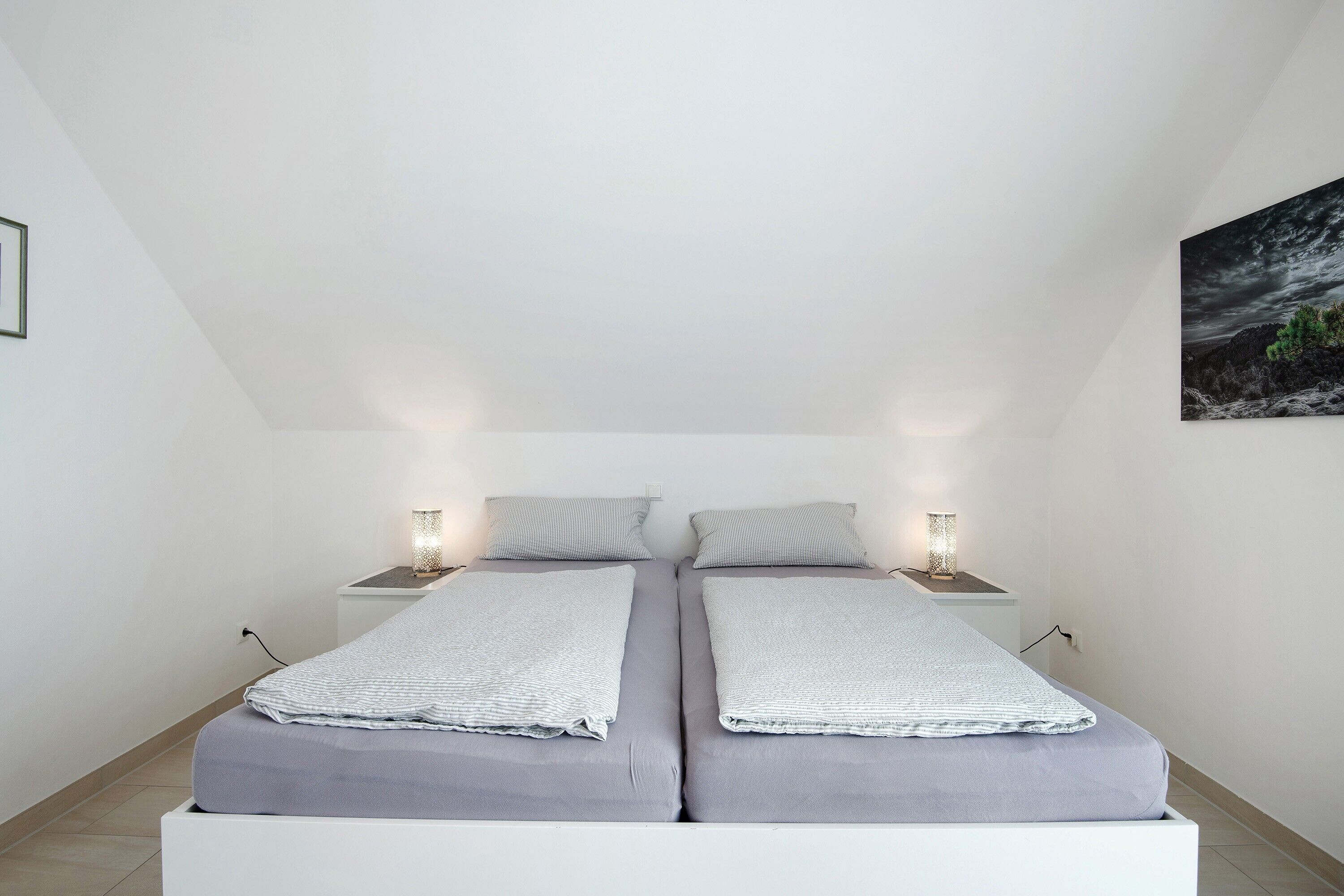 Una camera da letto con due letti, comodini con lampade e un quadro appeso al muro.