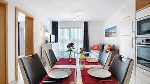 A modern dining area with a table set for four, a kitchen with a microwave and oven, and a view of a cityscape through the window.
