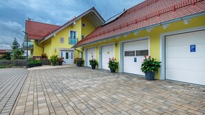 A yellow building with a red roof, multiple garage doors, and potted plants.