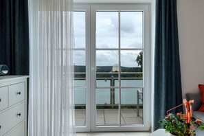 A room with a sliding glass door leading to a balcony with a view of a body of water and a distant building. - Apartment 'Rosi' with Balcony and Wi-Fi (Ihrlerstein)
