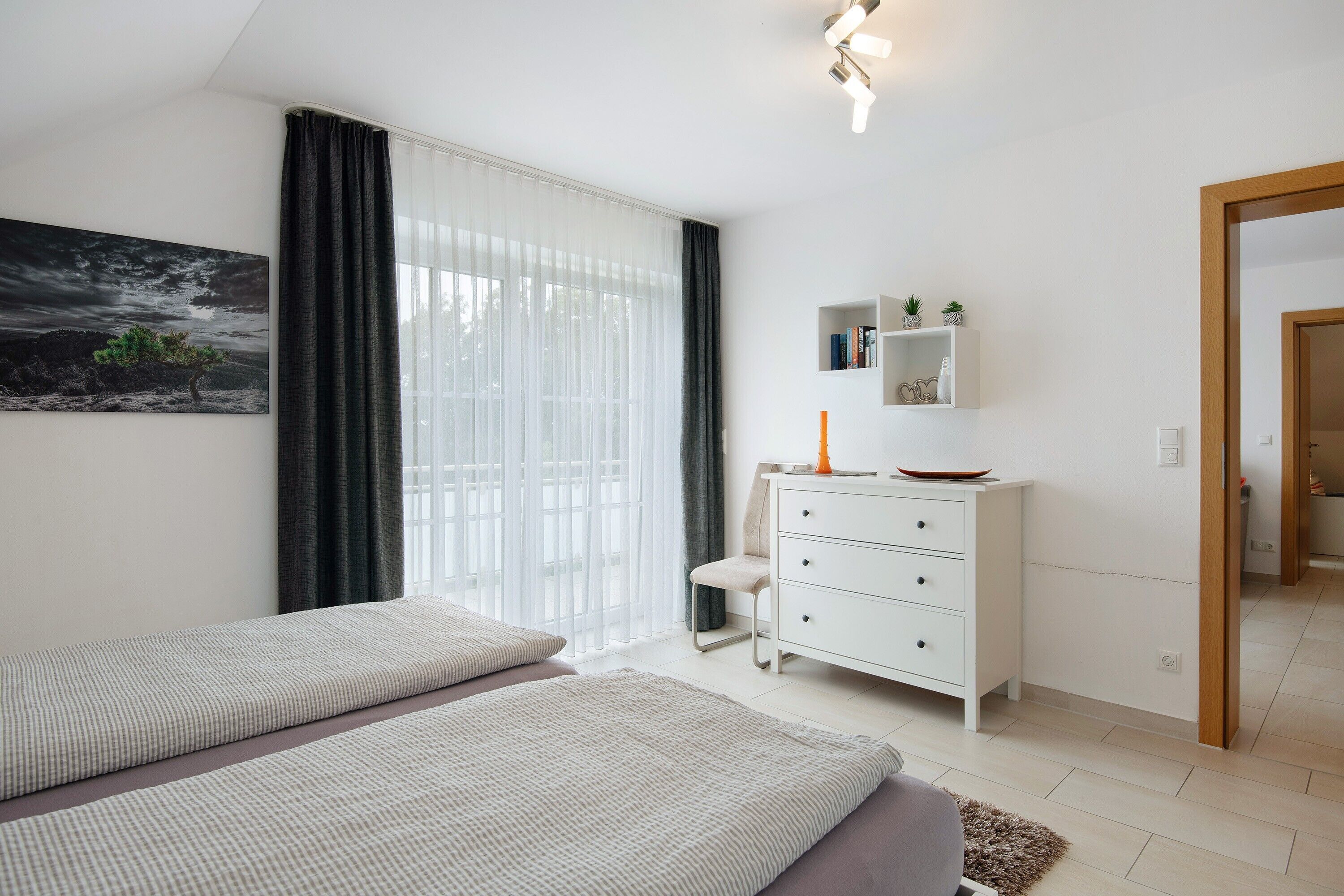 Ein modernes Schlafzimmer mit zwei Betten, einer weißen Kommode, einem Regal mit Pflanzen und einem Bild an der Wand.