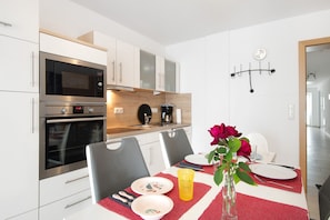 A modern kitchen with stainless steel appliances, a dining table set with plates, a vase with flowers, and a clock on the wall. - Apartment 'Rosi' with Balcony and Wi-Fi (Ihrlerstein)