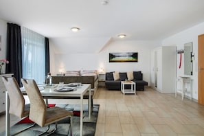 A modern living room with a dining area, a sofa set, a painting on the wall, and a door with a coat rack. - Studio Apartment 'Mia' with Mountain View, Balcony, and Wi-Fi (Ihrlerstein)
