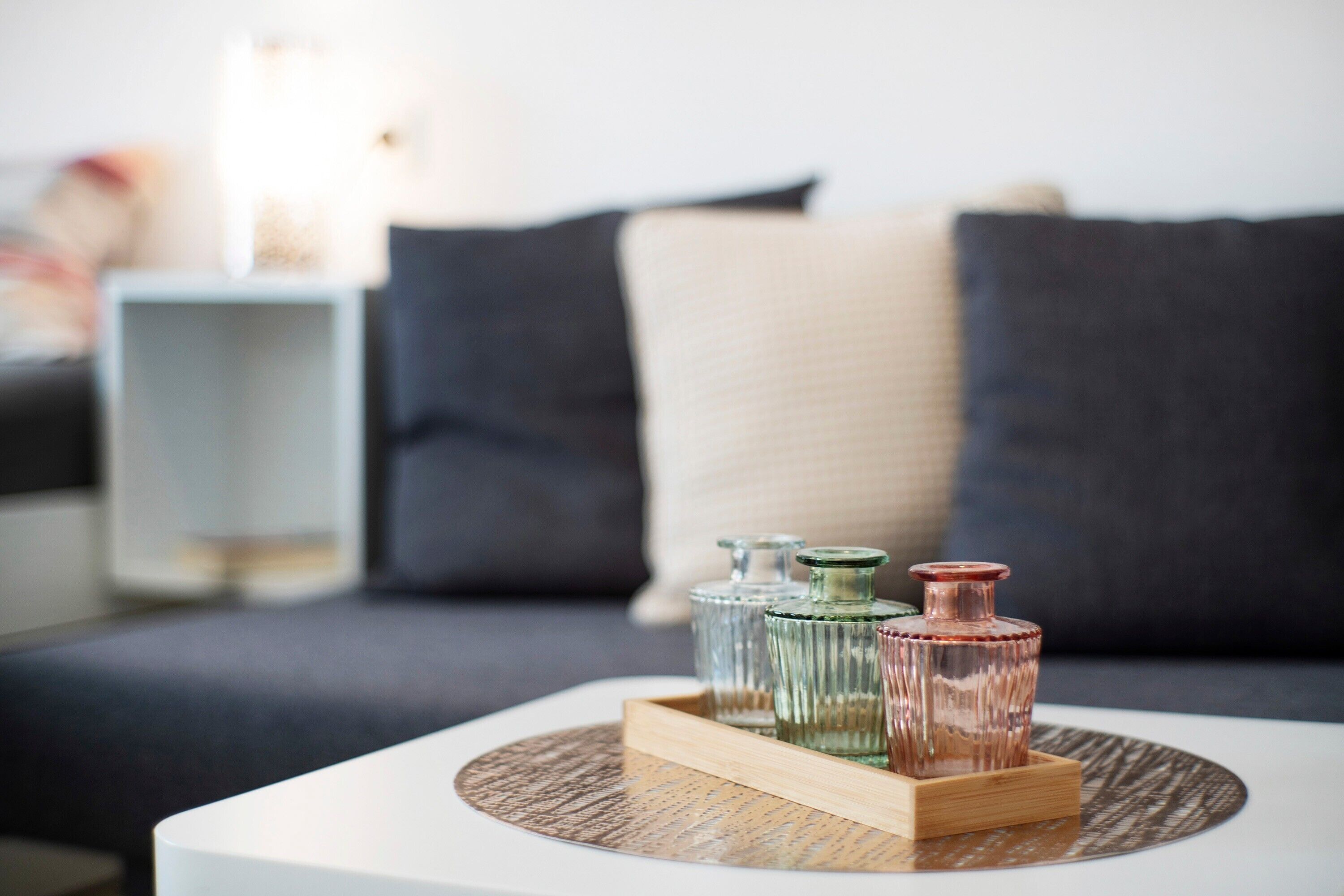 A modern living room with a white coffee table, a tray with glass containers, and a sofa with dark cushions.