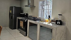 Eine moderne Küche mit einem Gasherd, einem Backofen, einem Kühlschrank, einem Fenster und einer Arbeitsplatte mit einem Mixer.