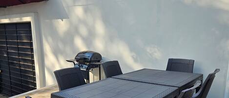 Une terrasse avec une table et des chaises, un barbecue et un sol carrelé.