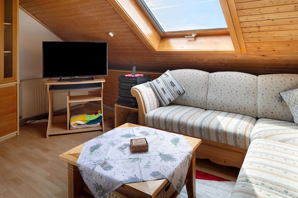 A cozy room with a wooden ceiling, a sofa, a television, and a small table with a tablecloth.