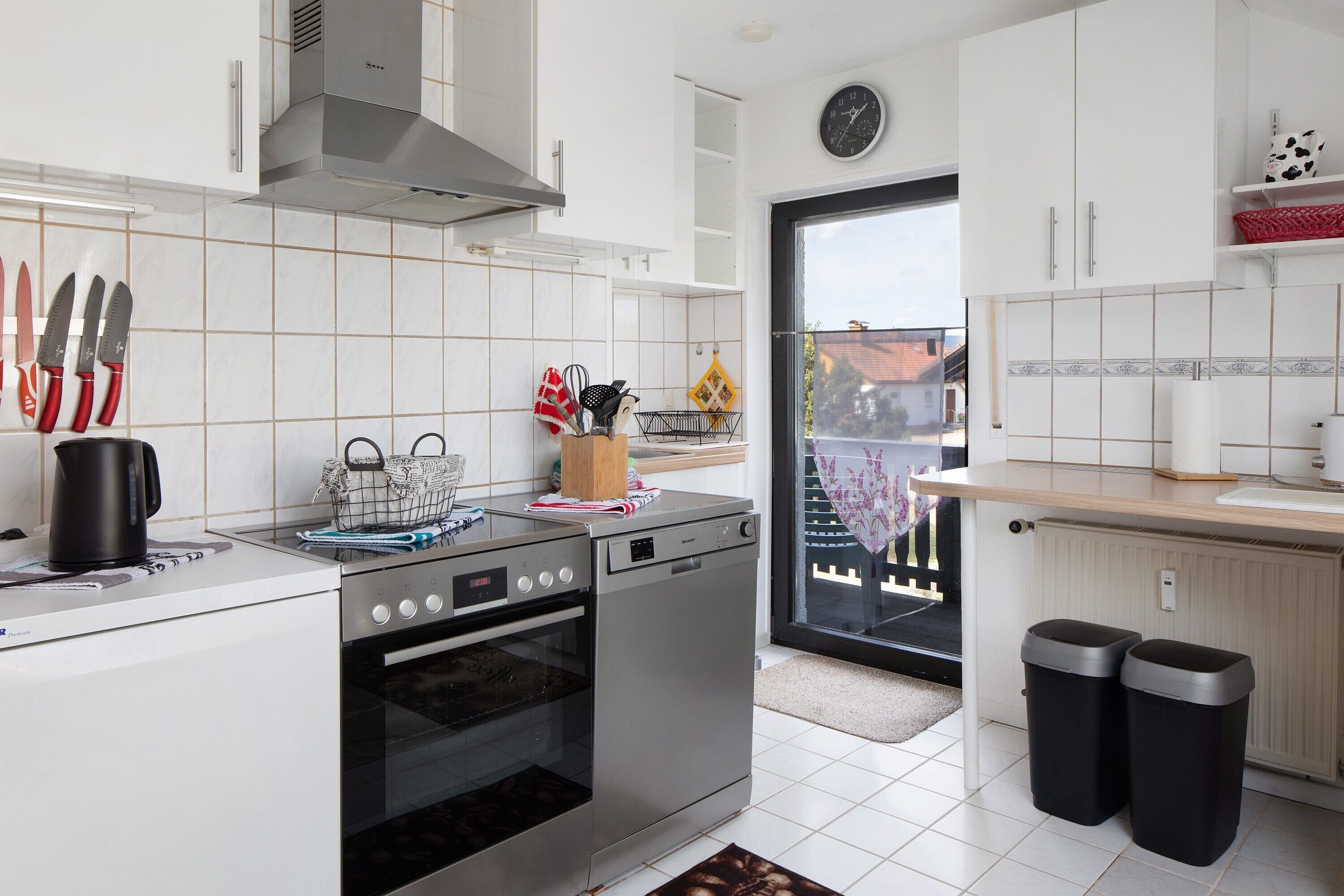 Una cocina moderna con armarios blancos, electrodomésticos de acero inoxidable y vistas a través de un ventanal.