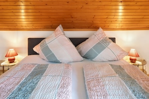 A bed with a patterned quilt, two pillows, a wooden ceiling, and two bedside lamps.