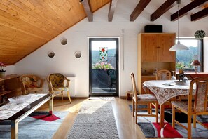 A dining area with a table and chairs, a wooden ceiling, and a view through a glass door.