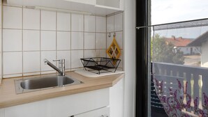 Ett kök med en diskho, ett fönster med utsikt över en balkong och ett vitt skåp.