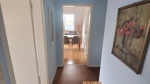 En hall med ett mattbeklätt golv, en bänk, en dörr och en tavla på väggen.