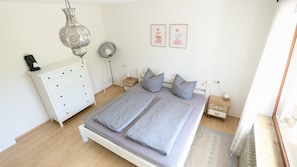 Une chambre à coucher comprenant un lit, une commode, des tables de chevet et une lampe suspendue.