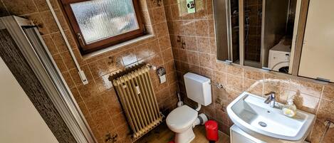Un baño con inodoro, radiador, ventana e lavabo.