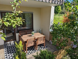 Une terrasse avec une table et des chaises en bois, un sol à carreaux et une vue sur un jardin.