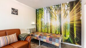 Een kamer met een bruine leren bank, een geborduurde bed, een bosdecoratie op de muur en een klein, ingelijst fotootje aan de wand.