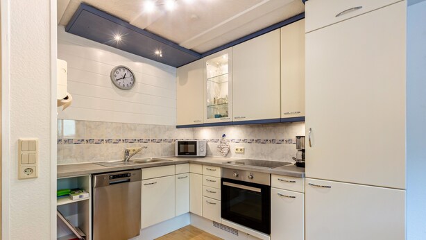Een moderne keuken met witte kasten, een magnetron, een vaatwasser en een klok aan de muur.