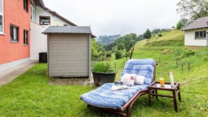 Een lounge stoel met een boek, zonnebril, een glas sinaasappelsap en een flesje op een bijzettafeltje.