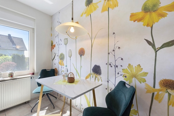 Ein Essbereich mit Tisch, Stühlen, einer Hängelampe und einer Wand mit Blumenmuster-Tapete.