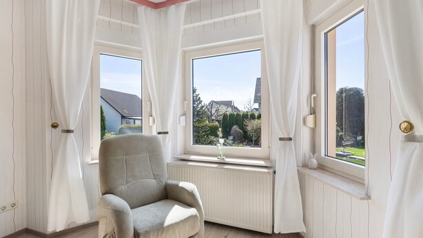 Una habitación con radiador, una silla y dos ventanas con cortinas.