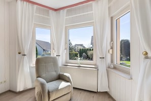 Ein Zimmer mit Heizkörper, einem Sessel und zwei mit Vorhängen versehenen Fenstern.