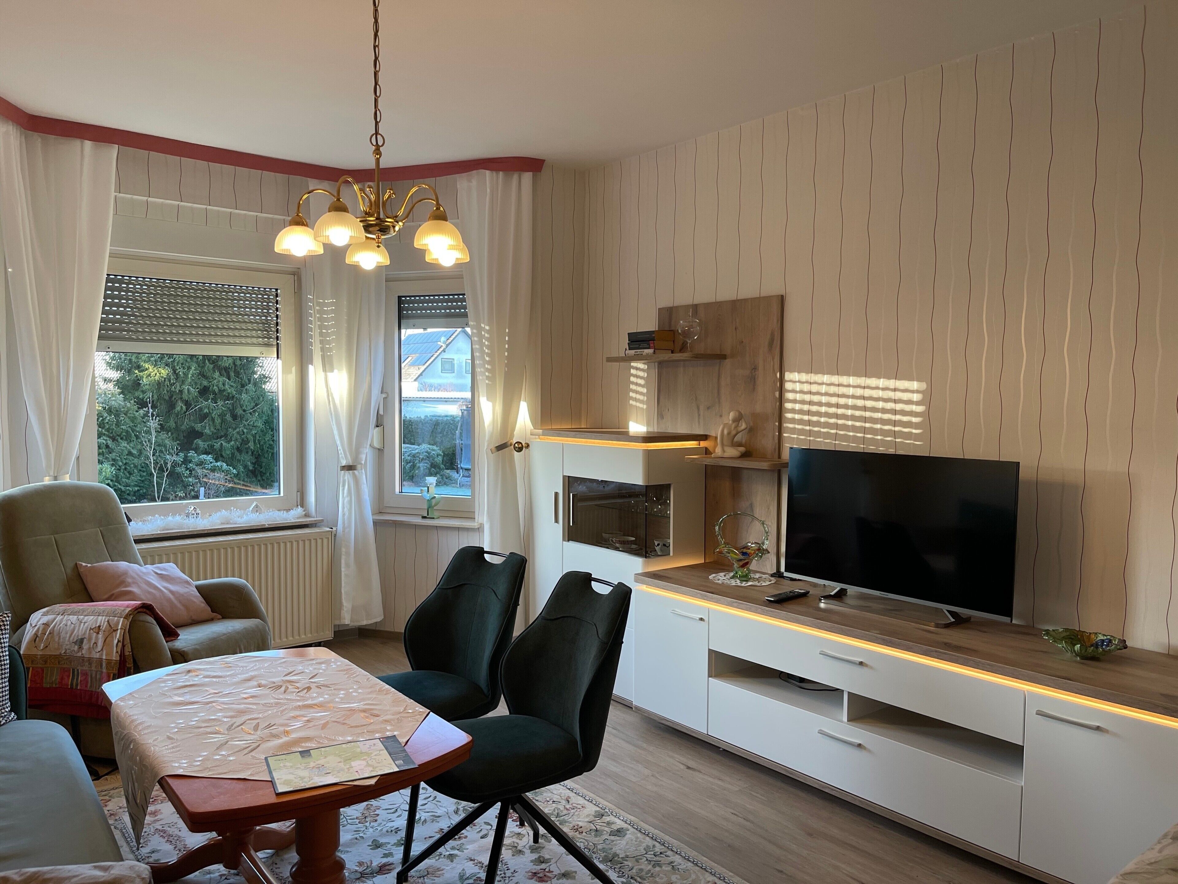 Una sala moderna con comedor, televisor y ventana con cortinas.