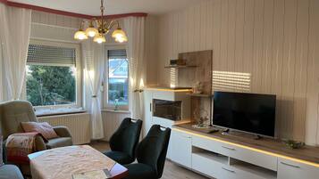 Una sala moderna con comedor, televisor y ventana con cortinas.