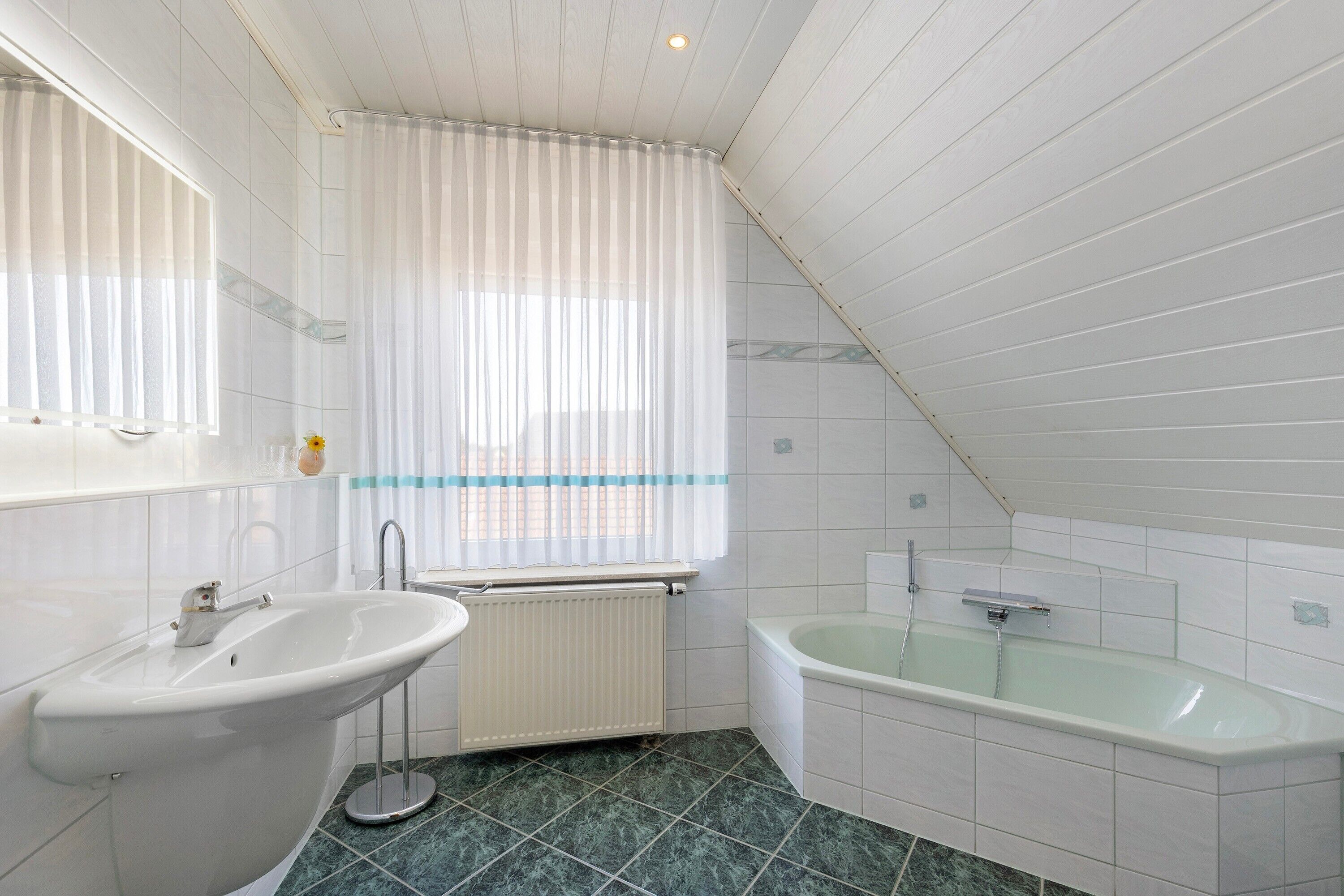 Un baño con lavabo, bañera y ventana con cortinas.