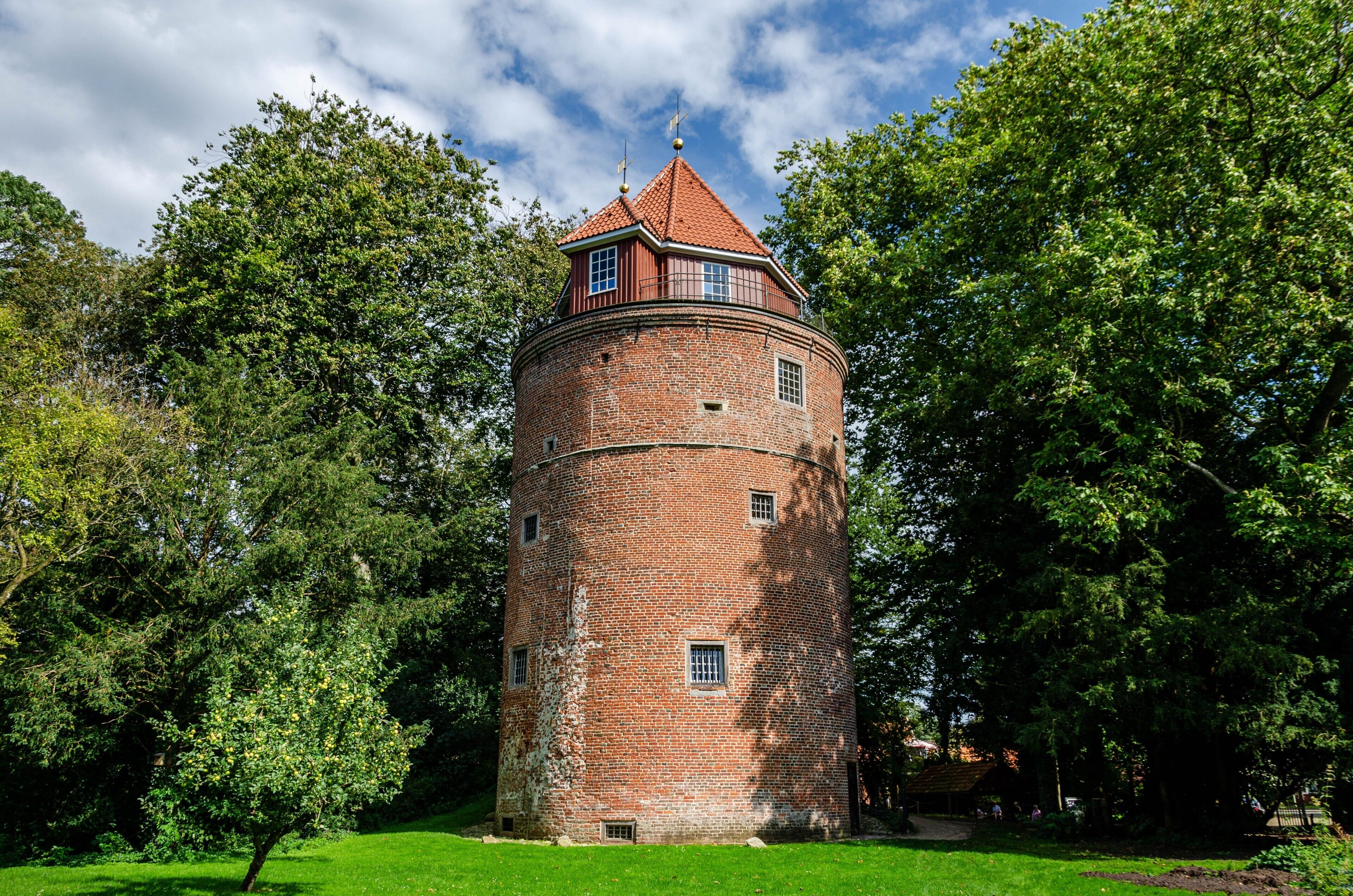 A brick tower with a conical roof, surrounded by lush greenery.
