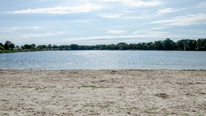 Una playa arenosa con un lago tranquilo y una orilla bordeada de bosque.