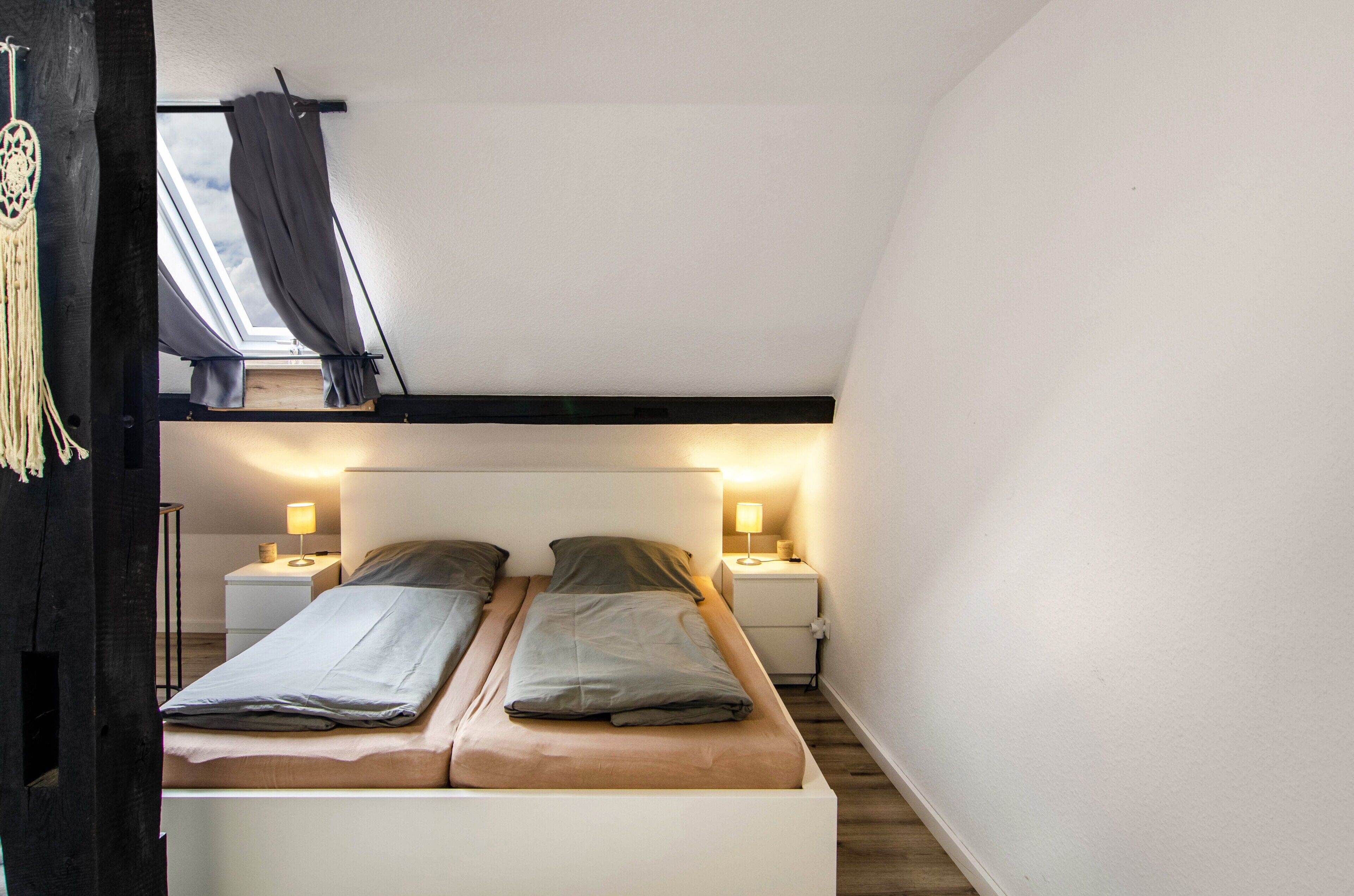 A bedroom with two beds, bedside lamps, a skylight, and a macrame wall hanging.