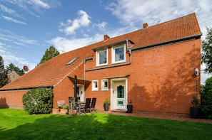 A red brick house with a tiled roof, a front door, and a small garden with a lawn and potted plants. - Apartment 'Lotte' with Shared Terrace, Shared Garden and Wi-Fi (Detern)