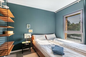 A bedroom with a bed, a nightstand, a lamp, and a window.