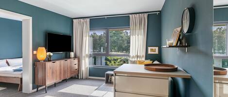 Un dormitorio moderno con cama, televisor, mueble de madera y un gran ventanal con cortinas.