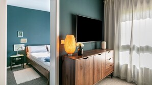 A bedroom with a bed, a dresser, a TV, and a window with curtains.