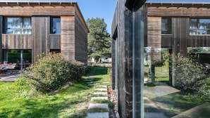 Un edificio moderno con paneles de madera, un área de estar al aire libre y un camino que lleva a la entrada.